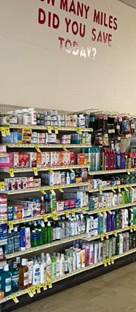 the medicine section of Hanna Hometown Market. Above the shelves are printed on the wall the words 'How many miles did you save today?'.